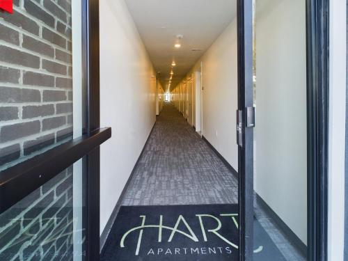 Apartments in Clearfield UT Long interior hallway with white walls and gray carpet, viewed from an open glass door. A Hart Apartments mat is visible at the entrance.