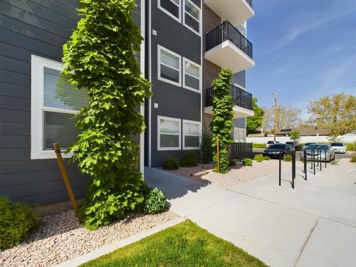 Apartments in Clearfield UT Exterior of a modern apartment building with gray siding, green plants, balconies, and a parking area with cars under a clear blue sky.