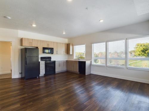 Apartments in Clearfield UT A spacious, unfurnished kitchen with wooden cabinets, black appliances, and hardwood flooring. Large windows provide ample natural light.