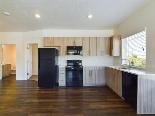 Apartments in Clearfield UT Modern kitchen with wood cabinets, black appliances, and a dark wood floor. It features a fridge, oven, microwave, and dishwasher with a window above the sink.